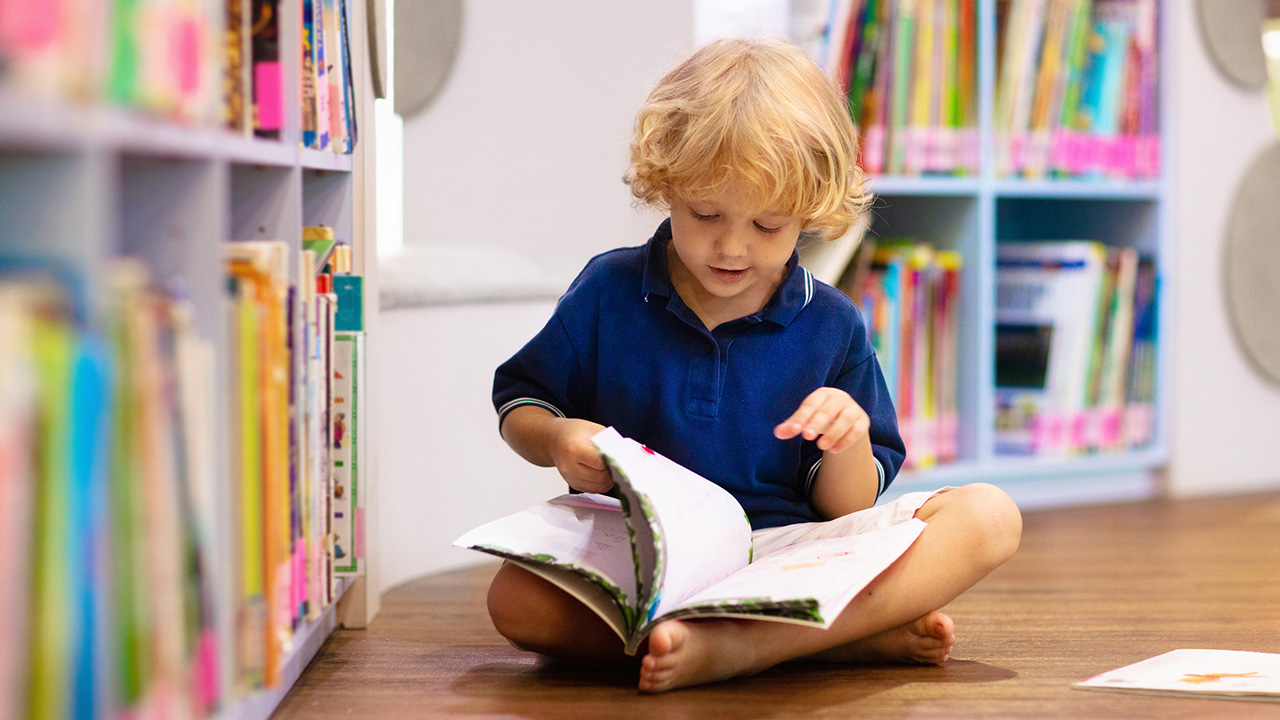 Child in the library reading a book. 